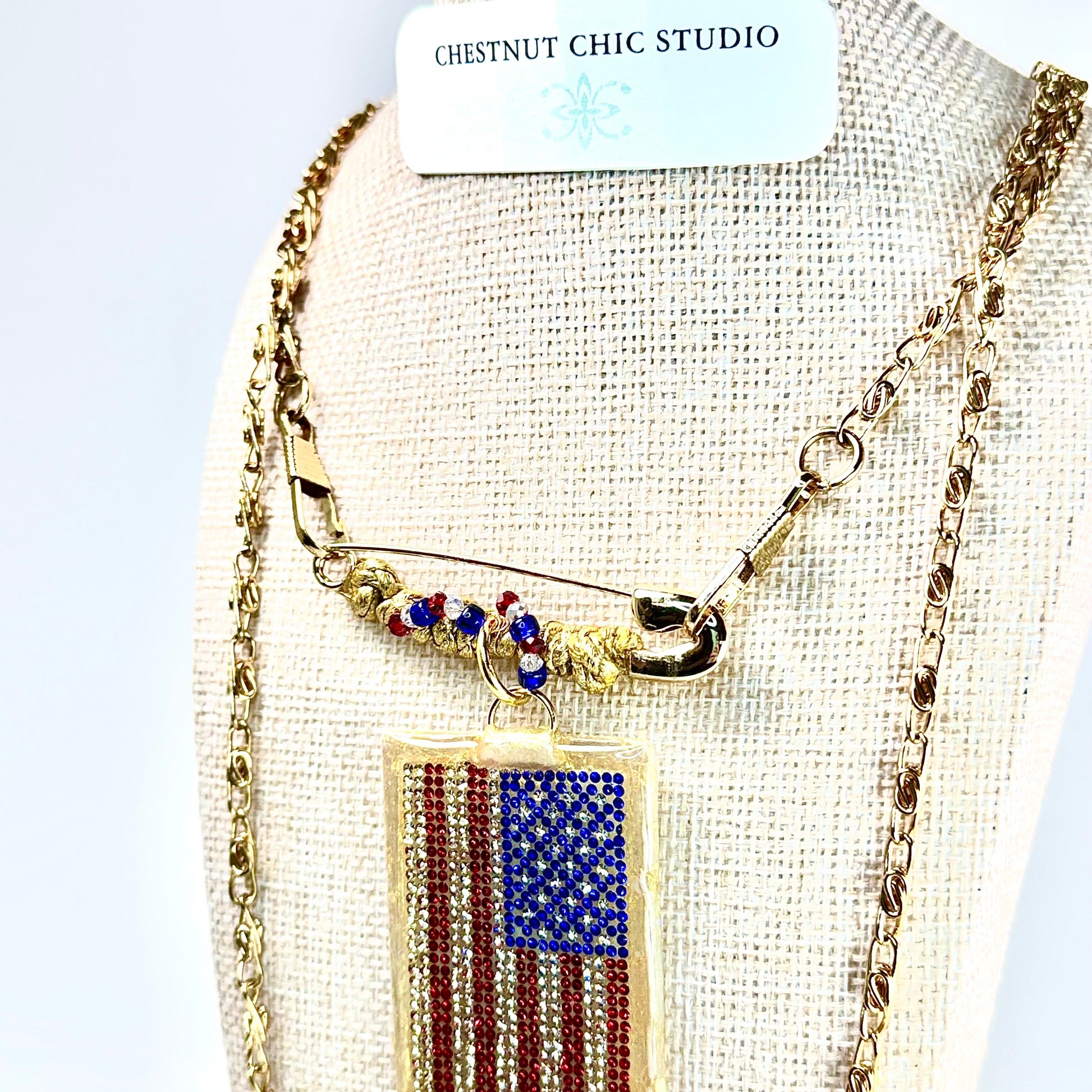 This one-of-a-kind, hand crafted artisan statement necklace is a convertible piece of jewelry that is a necklace, a brooch or pin, and a pendant. American flag is sparkling crystal with gold accents in leather, metal and vintage chain. Made in Conroe Texas by Chestnut Chic Studio. 