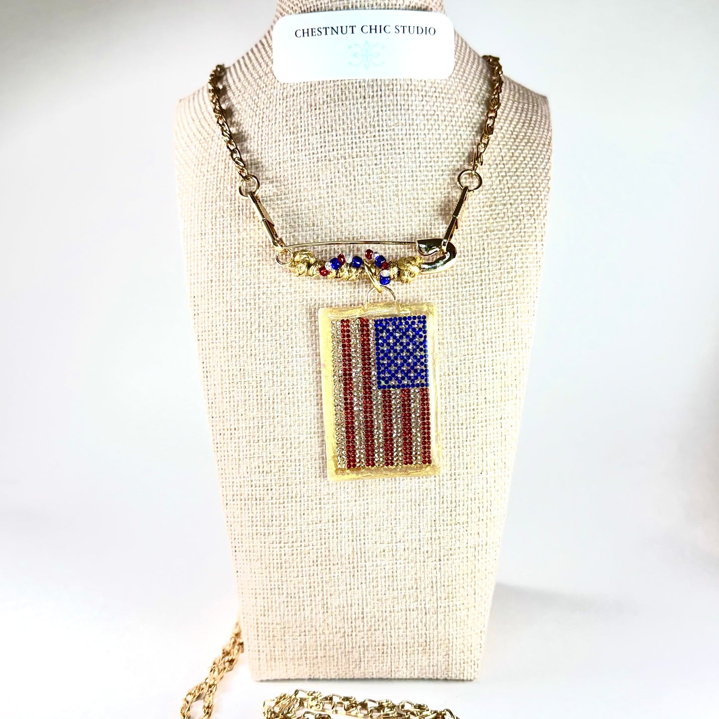 This one-of-a-kind, hand crafted artisan statement necklace is a convertible piece of jewelry that is a necklace, a brooch or pin, and a pendant. American flag is sparkling crystal with gold accents in leather, metal and vintage chain. Made in Conroe Texas by Chestnut Chic Studio. 