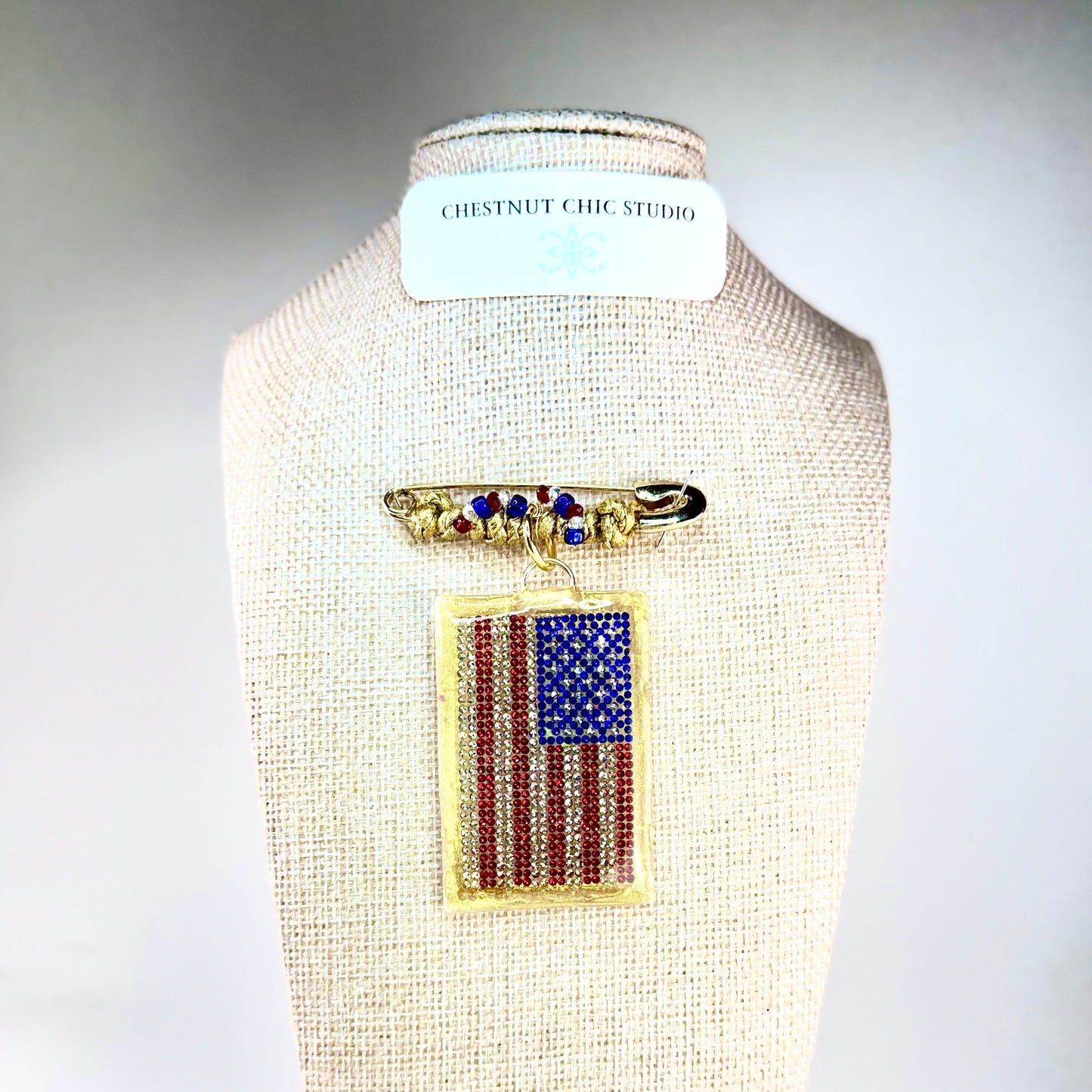 This one-of-a-kind, hand crafted artisan statement necklace is a convertible piece of jewelry that is a necklace, a brooch or pin, and a pendant. American flag is sparkling crystal with gold accents in leather, metal and vintage chain. Made in Conroe Texas by Chestnut Chic Studio. 