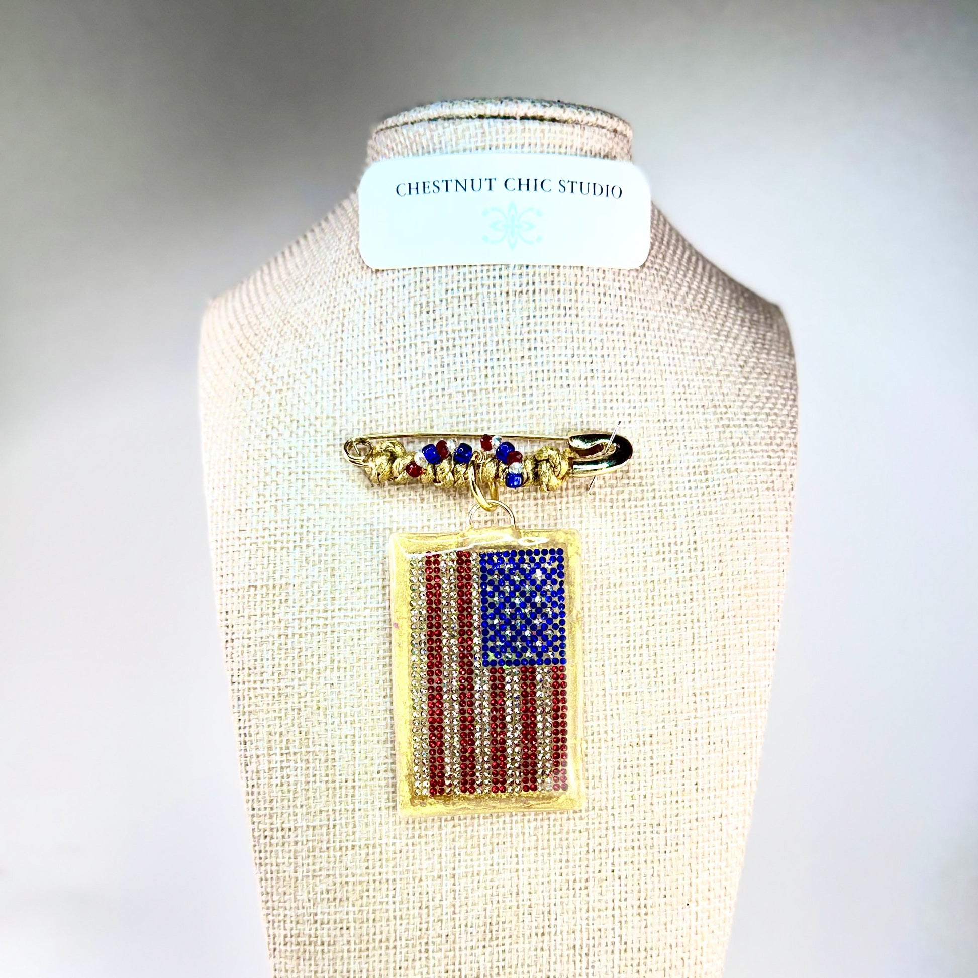 This one-of-a-kind, hand crafted artisan statement necklace is a convertible piece of jewelry that is a necklace, a brooch or pin, and a pendant. American flag is sparkling crystal with gold accents in leather, metal and vintage chain. Made in Conroe Texas by Chestnut Chic Studio. 