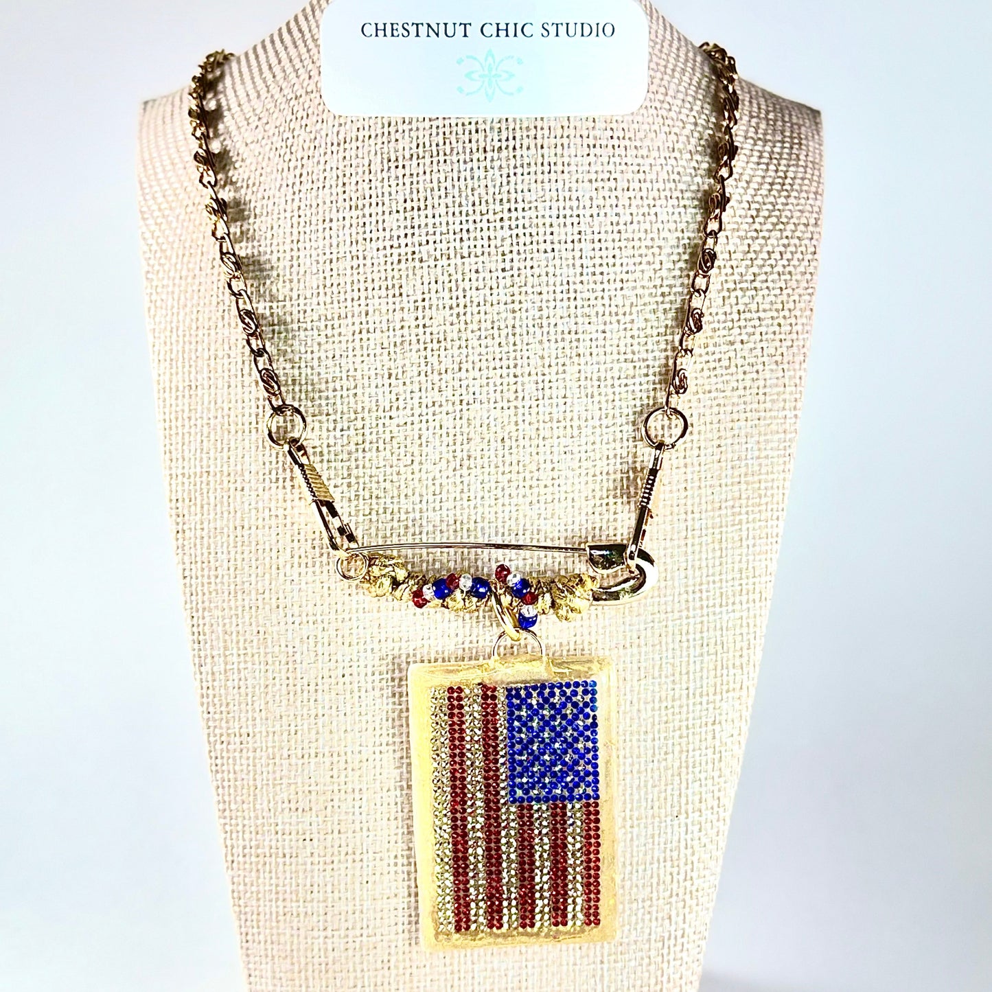 This one-of-a-kind, hand crafted artisan statement necklace is a convertible piece of jewelry that is a necklace, a brooch or pin, and a pendant. American flag is sparkling crystal with gold accents in leather, metal and vintage chain. Made in Conroe Texas by Chestnut Chic Studio. 