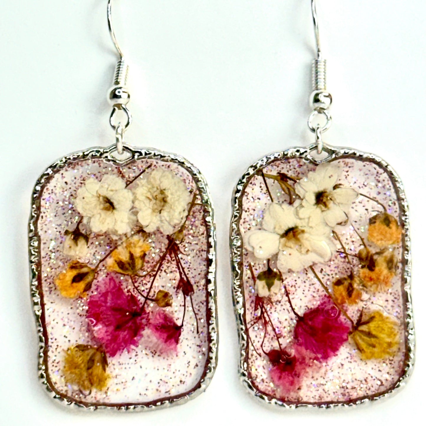 pressed flower earrings with mini buds in pink, yellow and white. Shimmering in a silver-tone setting. Make in Texas.