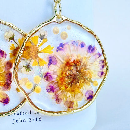 Close up hand pressed daisy flower earrings set in a gold-tone hoop with purple accents