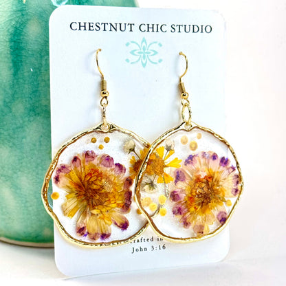 Hand pressed flower earrings with purple and yellow daisies set in a gold-tone hoop.